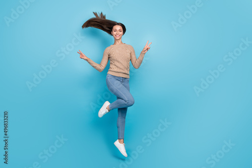Full length body size view of attractive cheerful girl jumping showing double v-sign isolated over bright blue color background