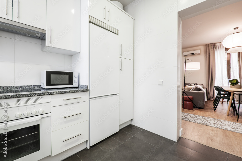 White kitchen with matching appliances, gray granite countertop, white microwave and walkout to living room and dining room White kitchen with matching appliances, gray granite countertop, white microwave and walkout to living room and dining room