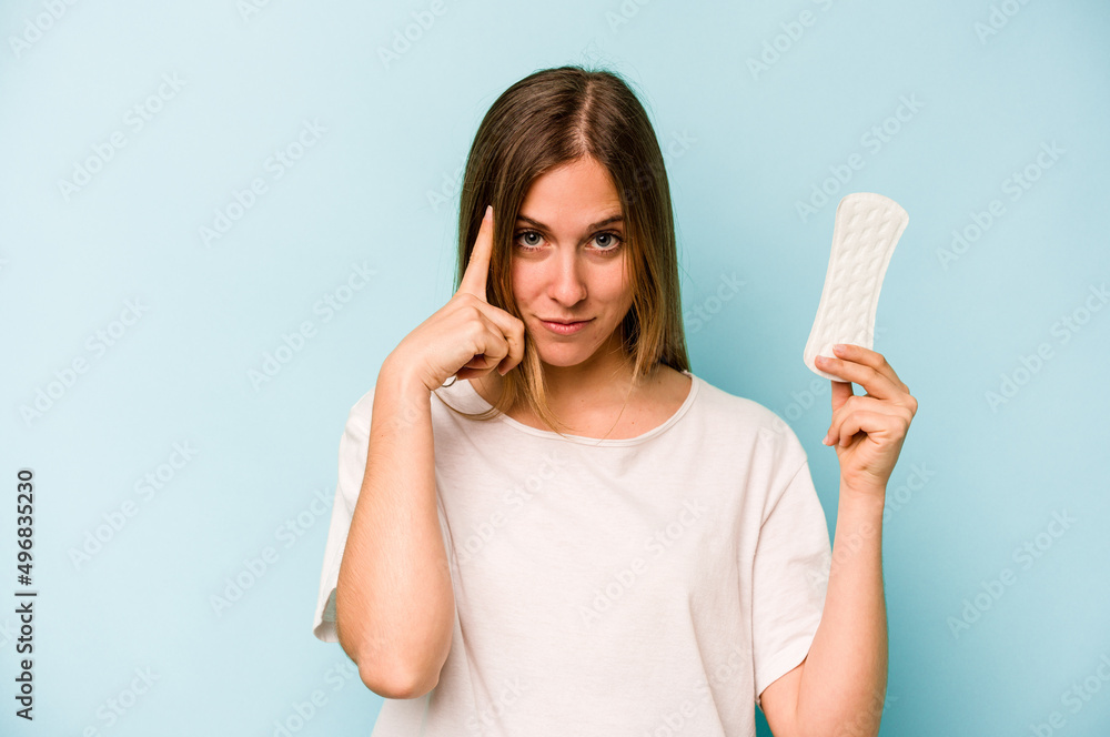 Young caucasian woman holding sanitary napkin isolated on blue background pointing temple with finger, thinking, focused on a task. Young caucasian woman holding sanitary napkin isolated on blue background pointing temple with finger, thinking, focused on a task.