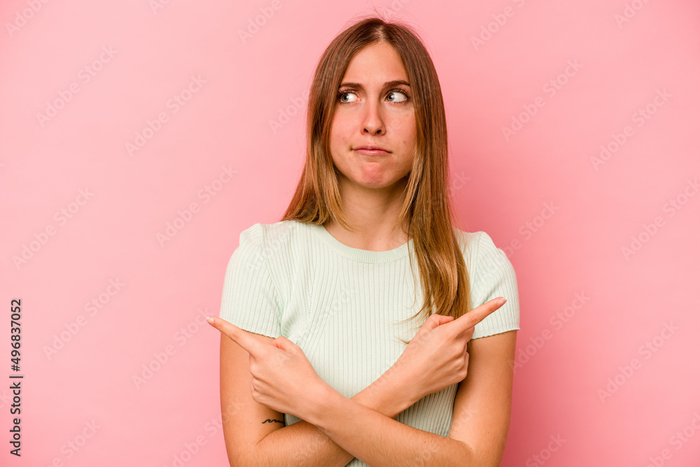 Young caucasian woman isolated on pink background points sideways, is trying to choose between two options. Young caucasian woman isolated on pink background points sideways, is trying to choose between two options.