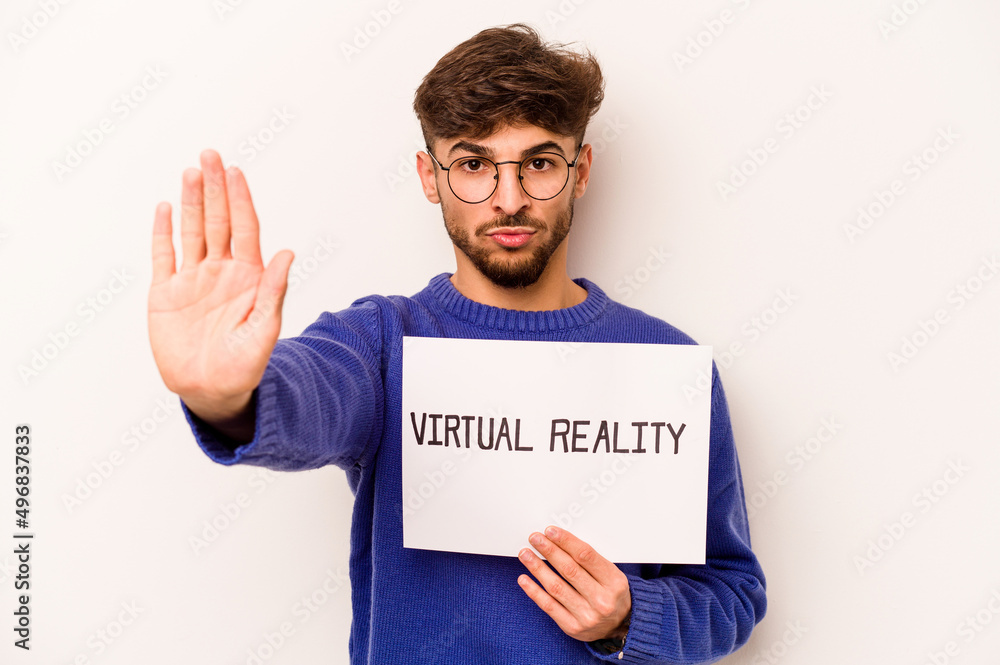 Young hispanic man holding a virtual reality placard isolated on white background standing with outstretched hand showing stop sign, preventing you. Young hispanic man holding a virtual reality placard isolated on white background standing with outstretched hand showing stop sign, preventing you.
