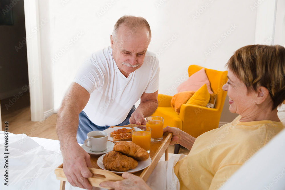 a loving elderly couple spend time together at home. healthy seniors lifestyle. relaxing at home. elderly man serves breakfast on a tray to his wife in bed