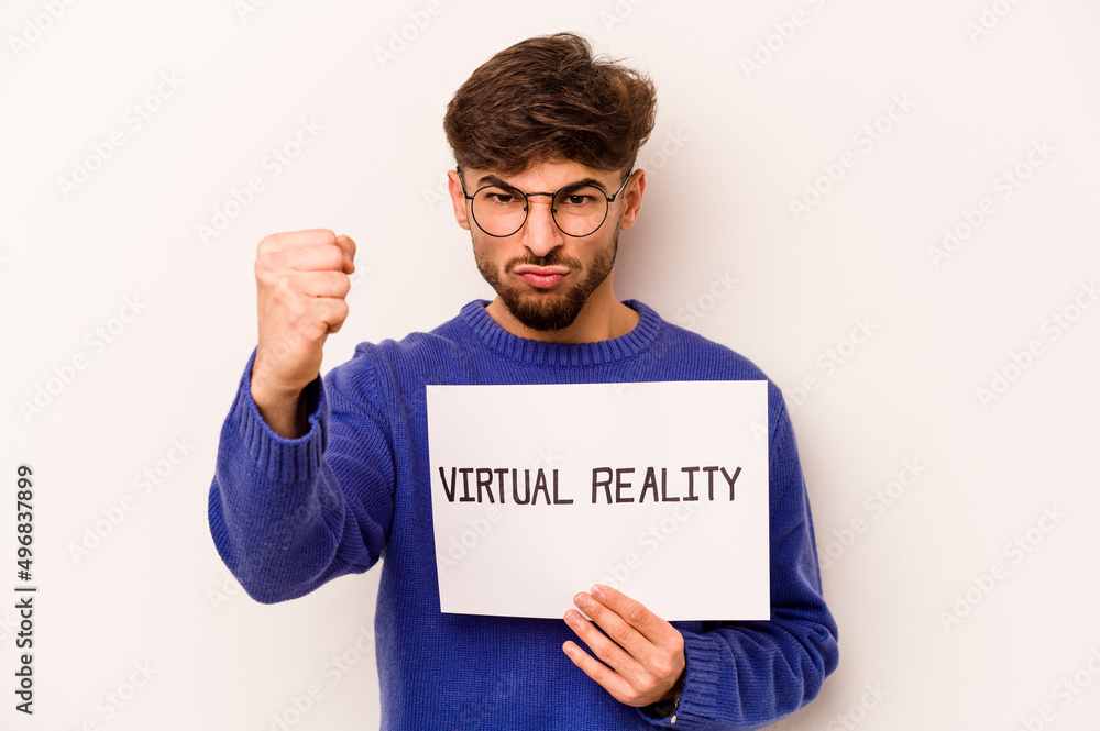 Young hispanic man holding a virtual reality placard isolated on white background showing fist to camera, aggressive facial expression. Young hispanic man holding a virtual reality placard isolated on white background showing fist to camera, aggressive facial expression.