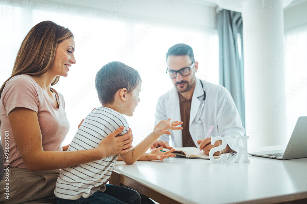 Smiling positive gp pediatrician in eyeglasses and medical uniform stroking shoulder of little boy patient, encouraging at clinic checkup. Young mother holding small kid son on laps, greeting doctor. Smiling positive gp pediatrician in eyeglasses and medical uniform stroking shoulder of little boy patient, encouraging at clinic checkup. Young mother holding small kid son on laps, greeting doctor.