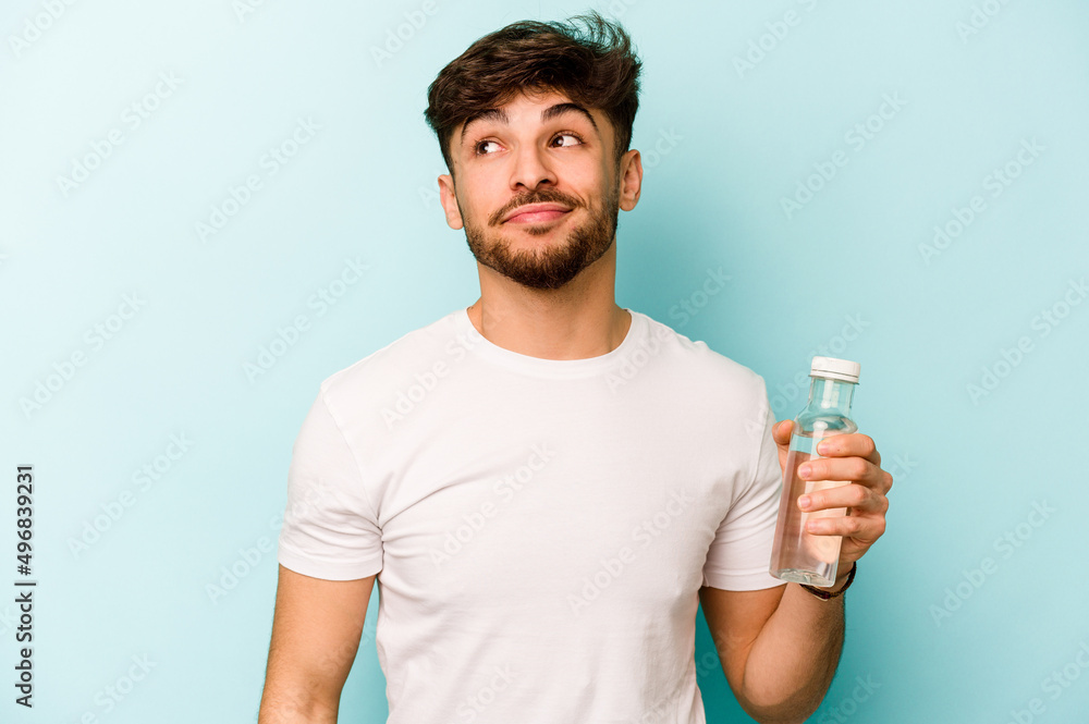 Young hispanic man holding a bottle of water isolated on white background dreaming of achieving goals and purposes Young hispanic man holding a bottle of water isolated on white background dreaming of achieving goals and purposes