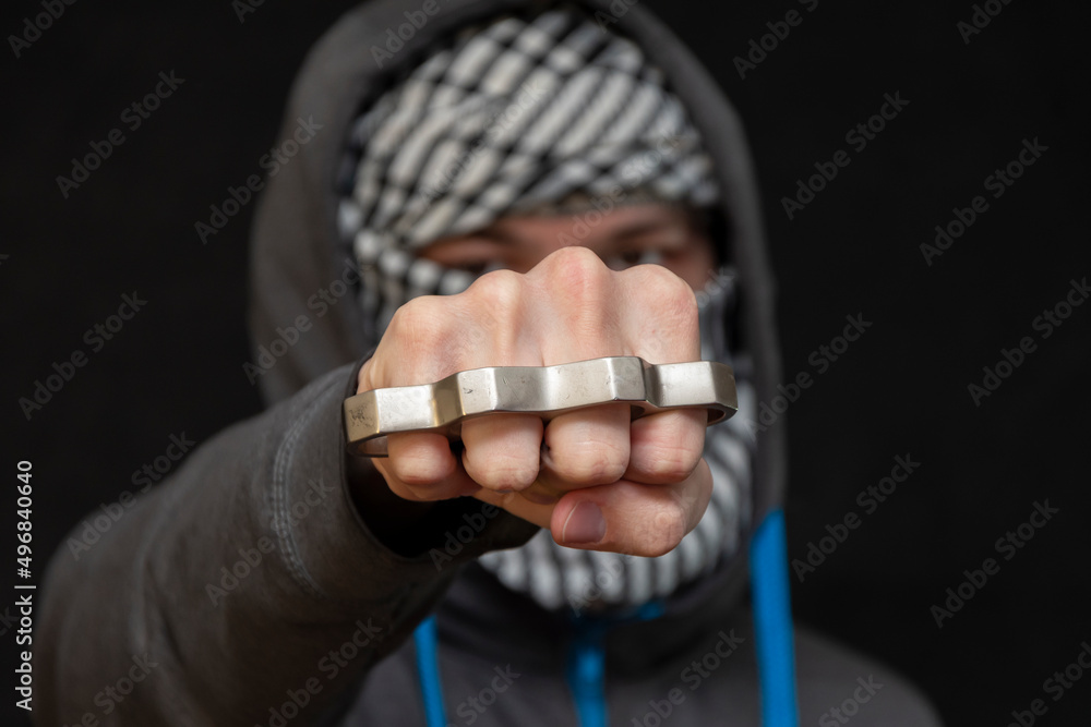 Brass knuckles in the hand of a man with a scarf covering his face on a