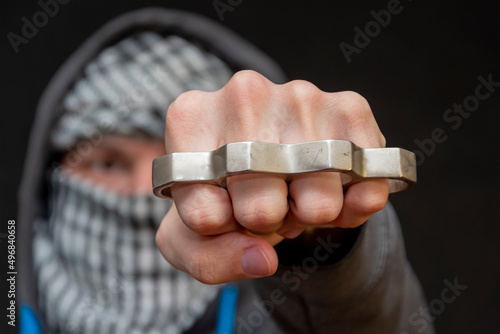 Metal brass knuckles in the hands of a man hiding his face,prohibited weapons in a fight, a strong blow, street thugs photo