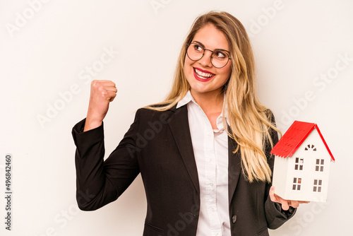Young business caucasian woman holding a toy house isolated on white background raising fist after a victory, winner concept.