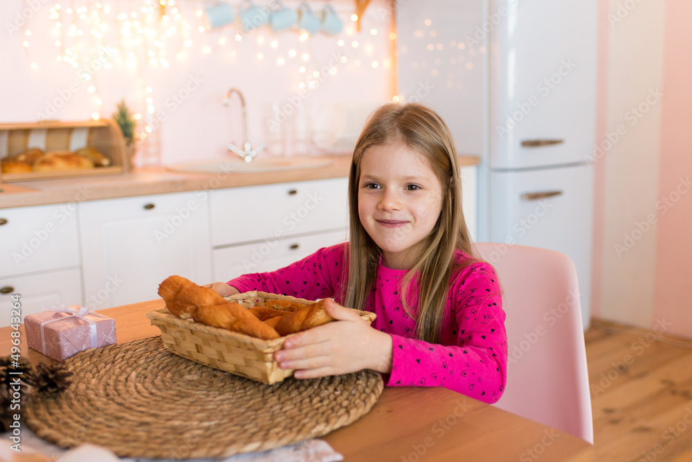 Cute smiling girl holding bread. Sits in the kitchen.
