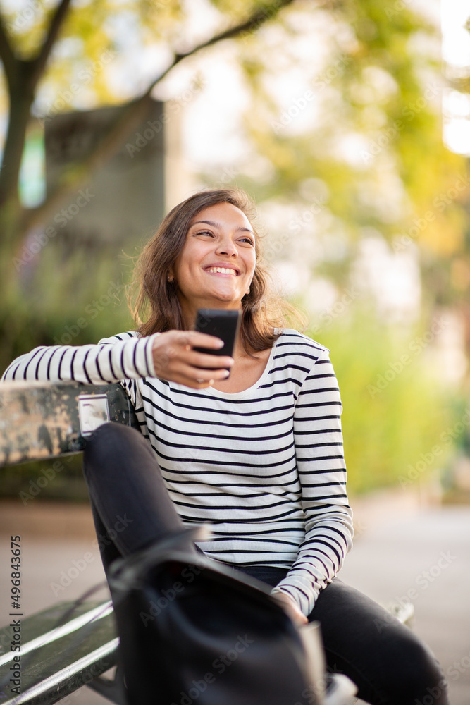 smiling young woman sitting on park bench with cellphone smiling young woman sitting on park bench with cellphone
