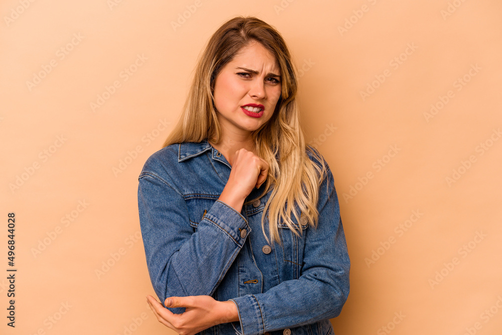 Young caucasian woman isolated on beige background massaging elbow, suffering after a bad movement. Young caucasian woman isolated on beige background massaging elbow, suffering after a bad movement.