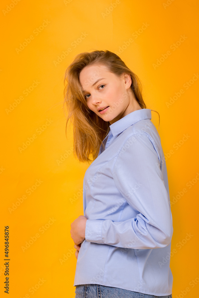 Positive emotions. Happy smiling girl in a blue shirt and blue jeans on a yellow background look at the camera. Color scheme of the Ukrainian flag.