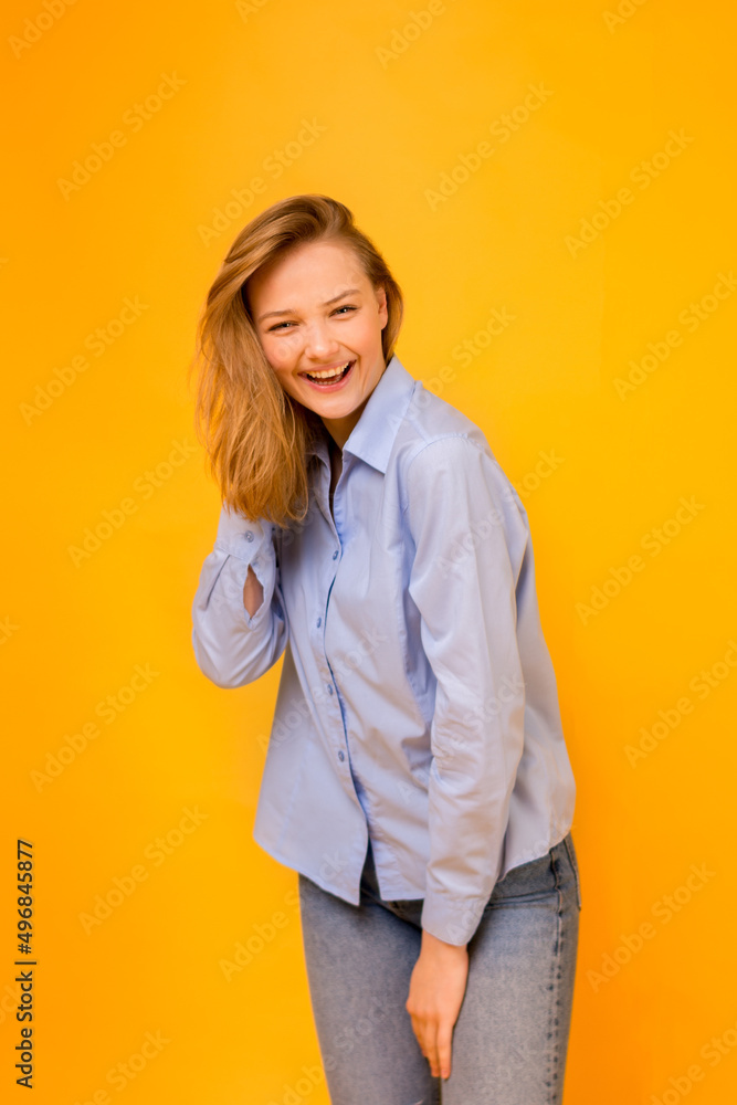 Emotions of happiness and success. Happy smiling girl in a blue shirt and blue jeans on a yellow background. Color scheme of the Ukrainian flag. Emotions of happiness and success. Happy smiling girl in a blue shirt and blue jeans on a yellow background. Color scheme of the Ukrainian flag.