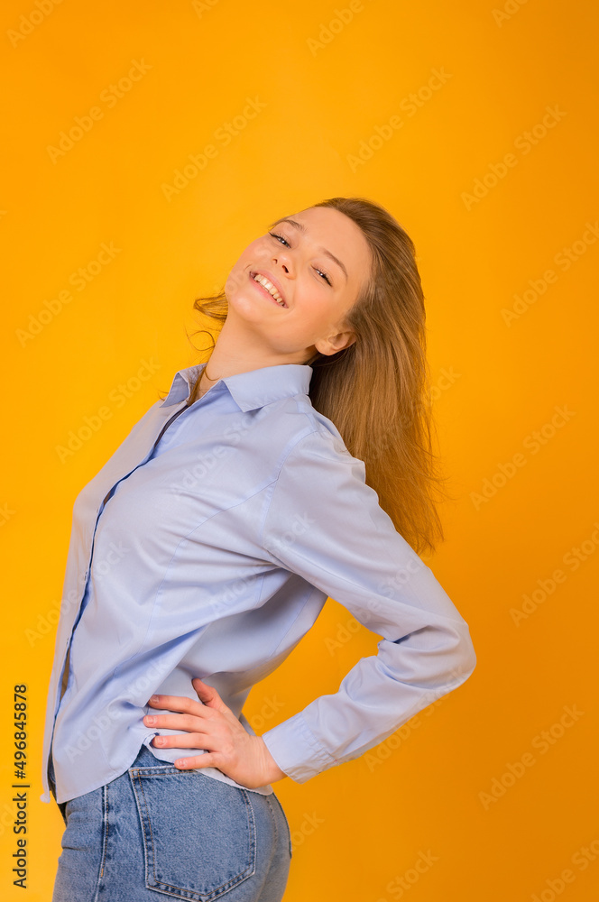 Emotions of happiness and success. Happy smiling girl in a blue shirt and blue jeans on a yellow background. Color scheme of the Ukrainian flag. Emotions of happiness and success. Happy smiling girl in a blue shirt and blue jeans on a yellow background. Color scheme of the Ukrainian flag.