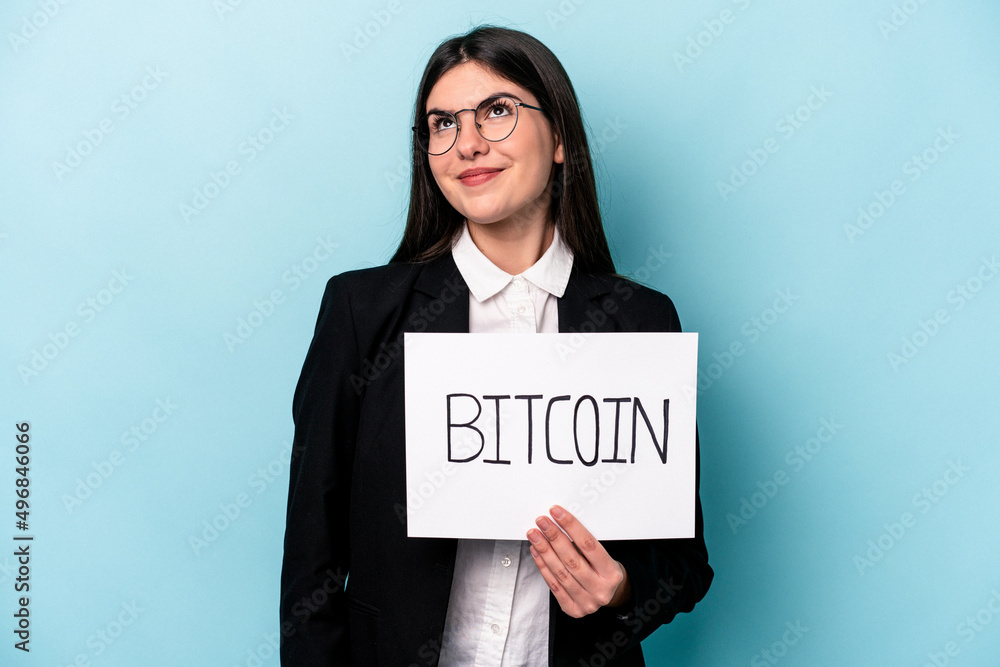 Young caucasian business woman holding a bitcoin placard isolated on blue background dreaming of achieving goals and purposes Young caucasian business woman holding a bitcoin placard isolated on blue background dreaming of achieving goals and purposes