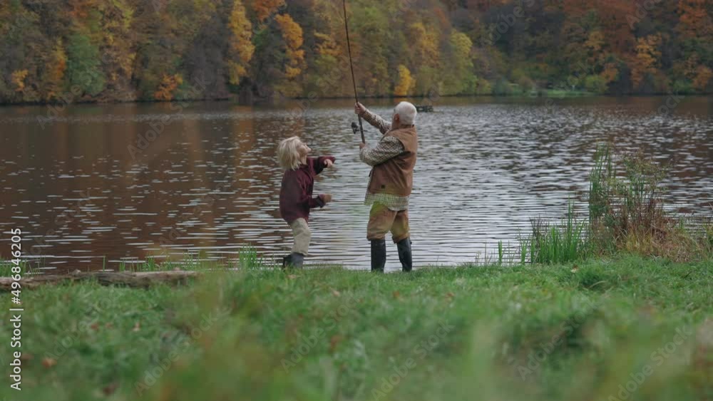 Grandson and grandfather in rubber boots fishing on lake Grandson and grandfather in rubber boots fishing on lake