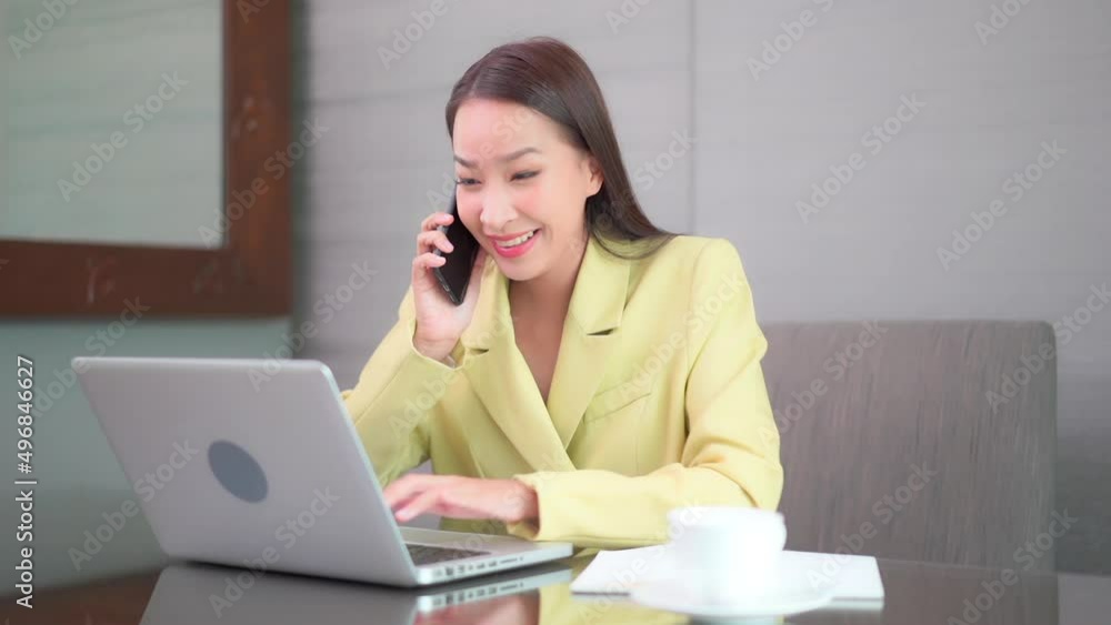A businesswoman with her smartphone in one hand while working on her laptop with the other smiles. A businesswoman with her smartphone in one hand while working on her laptop with the other smiles.