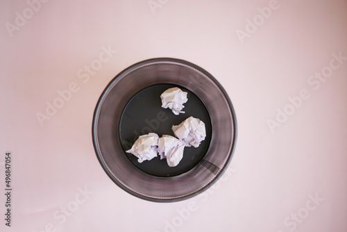 crumpled paper ball in a bin on a light purple background 
