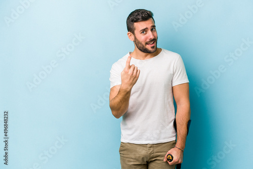 Young man with crutches isolated on blue background pointing with finger at you as if inviting come closer.