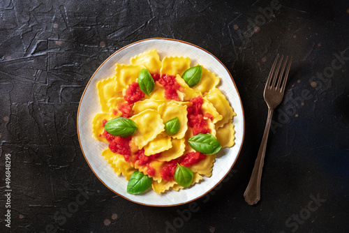 Ravioli with tomato sauce and fresh basil on a plate. Healthy Italian meal, overhead shot on a black slate background