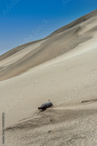 Glass bottle lying on the sand dune near the beach with blue sky. Let's take care of the planet © fotosdanielgbueno