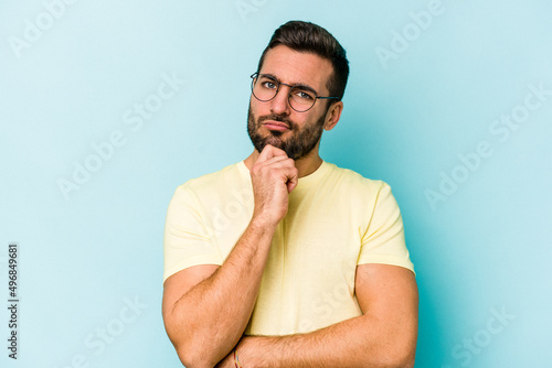 Fototapeta Young caucasian man isolated on blue background thinking and looking up, being reflective, contemplating, having a fantasy