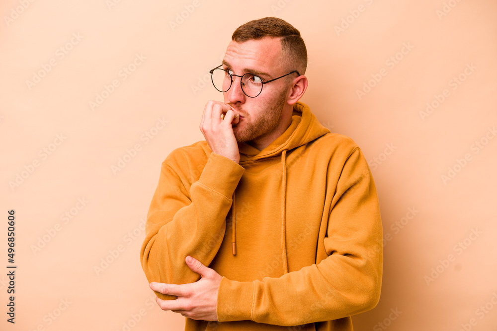 Young caucasian man isolated on beige background biting fingernails, nervous and very anxious. Young caucasian man isolated on beige background biting fingernails, nervous and very anxious.
