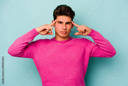 Young caucasian man isolated on blue background focused on a task, keeping forefingers pointing head.