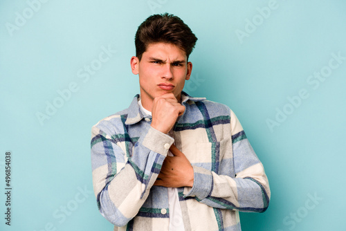 Young caucasian man isolated on blue background thinking and looking up, being reflective, contemplating, having a fantasy.