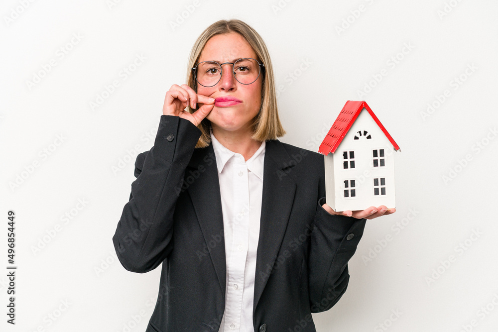 Young business caucasian woman holding a toy house isolated on white background with fingers on lips keeping a secret. Young business caucasian woman holding a toy house isolated on white background with fingers on lips keeping a secret.