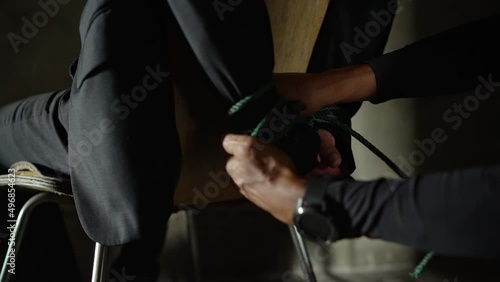 A hostage sitting on a chair was robbed by terrorists. Rope tied at hands for ransom in prison