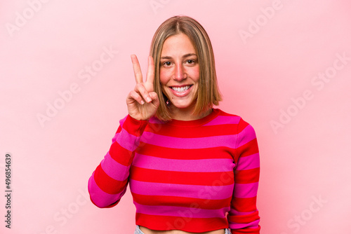 Young caucasian woman isolated on pink background showing victory sign and smiling broadly.