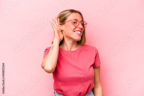 Young caucasian woman isolated on pink background trying to listening a gossip. © Asier