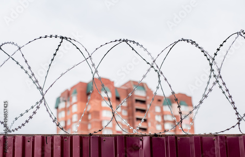 Barbed wire on fence with modern residential building on background. Protection and prohibition concept.