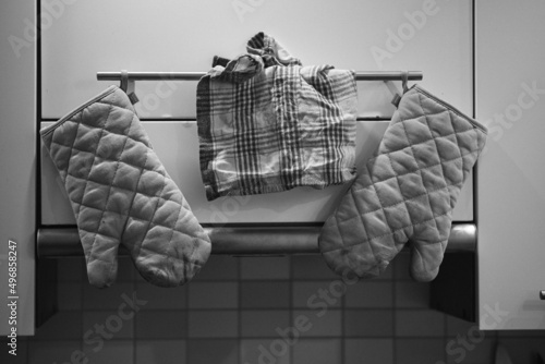 Grayscale shot of two oven mitts and a towel hanging on a kitchen rack photo