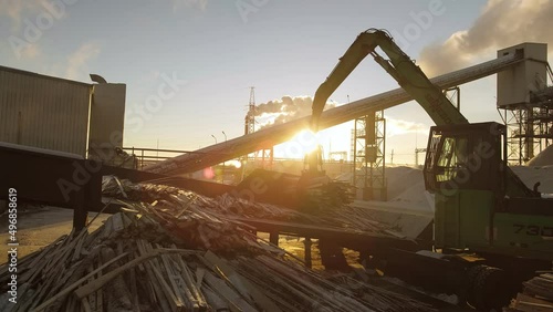 A track material handler is loading logs onto a conveyor at the factory
