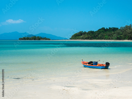 Scenic view of Koh Mak Island peaceful white sand beach with crystal clear turquoise water and local fishing boat against clear blue sky. Trat, Thailand.