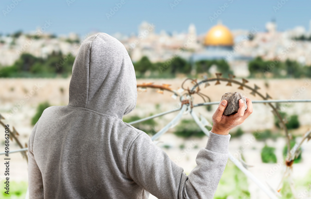 Fototapeta premium Rear view of a hooded person throwing stones at a metal balla in jerusalem