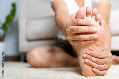 Foot pain, Asian woman feeling pain in her foot at home, female suffering from feet ache use hand massage relax muscle from soles in home interior, Healthcare problems and podiatry medical concept © sorapop