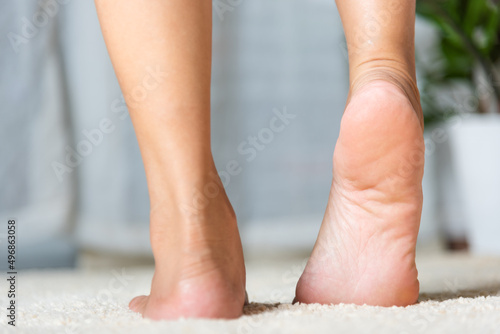 Foot pain, Asian woman standing feeling pain in her foot at home, female suffering from feet ache use hand massage relax muscle from soles in home interior, Healthcare problems and podiatry medical photo