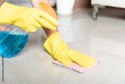 Asian woman wearing yellow rubber glover with cloth rag and detergent spray cleaning floor at home in living room  Female hands wash cleaner  housework and housekeeping concept