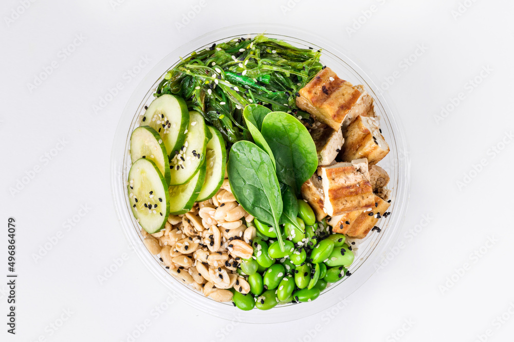 Poke bowl with rice, tofu, edamame beans, cucumber, chukka, spinach and peanuts on a white background. Plastic tableware for delivery. Top view. Poke bowl with rice, tofu, edamame beans, cucumber, chukka, spinach and peanuts on a white background. Plastic tableware for delivery. Top view.