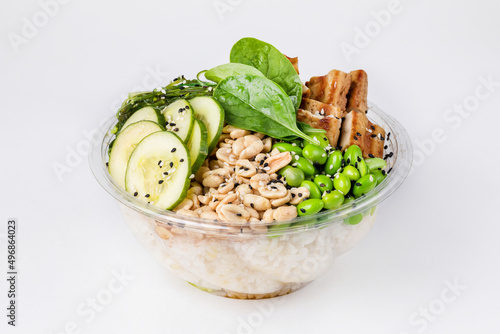 Poke bowl with rice, tofu, edamame beans, spinach and peanuts on a white background.  Plastic tableware for delivery. Close up. photo