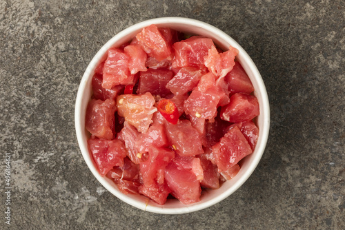 A bowl of sliced tuna in soy sauce on a gray textured background. Top view.