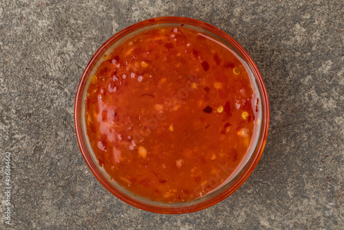 A cup with sweet chili sauce. Gray textured  background. Top view.