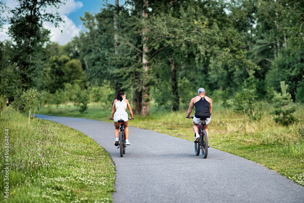 A man and a woman riding their bicycles in a park in summer in the sunny morning.
