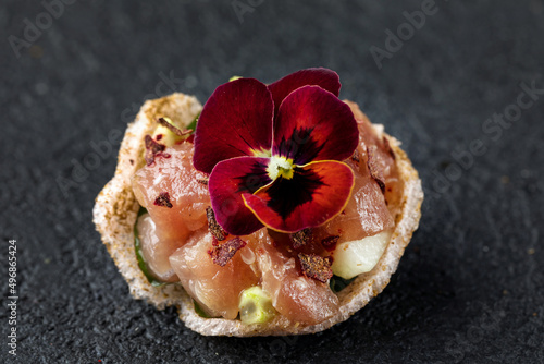 Tapas with guacamole, salmon tartare and viola flower. Dark gray textured background. Close up.