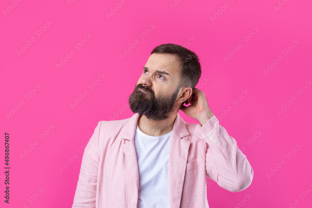 Fototapeta premium Handsome man with a beard in a pink jacket is thinking over an isolated red background.