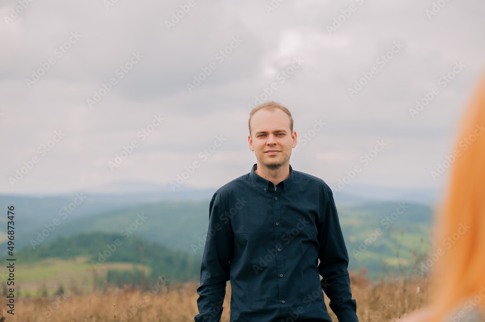 A handsome young guy looks in love at his wife, surrounded by beautiful views of the Carpathian mountains A handsome young guy looks in love at his wife, surrounded by beautiful views of the Carpathian mountains