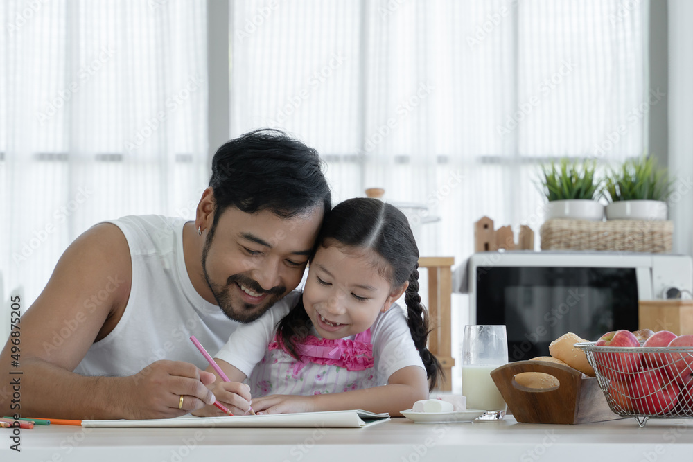 Happy Asian young father with beard and little cute daughter enjoy drawing with colored pencil together at home with glass of milk, marshmallows, breads and red apples on kitchen table Happy Asian young father with beard and little cute daughter enjoy drawing with colored pencil together at home with glass of milk, marshmallows, breads and red apples on kitchen table